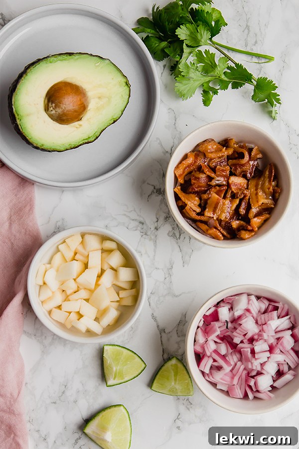 A flat lay photograph showcasing the individual ingredients required for Apple Bacon Guacamole, including avocados, apples, bacon, red onion, and lime.