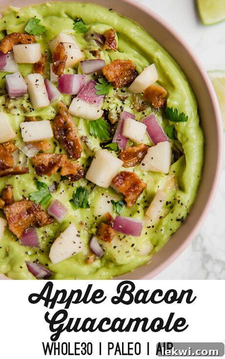 A full bowl of Apple Bacon Guacamole ready for dipping, with various chips and vegetables surrounding it on a rustic wooden table.