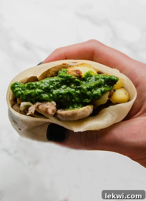 A hand holding a sausage breakfast burrito ready to be eaten.