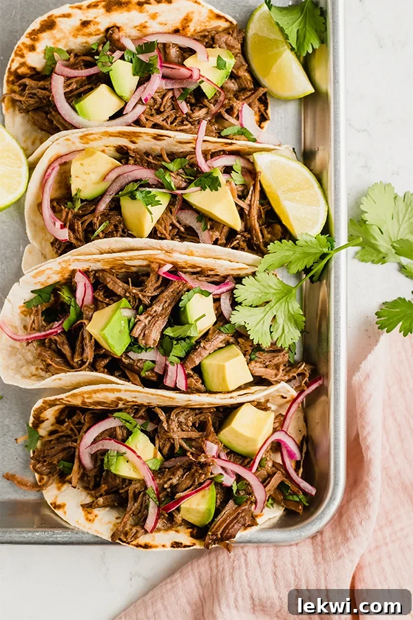 Delicious shredded beef tacos topped with fresh red onion, a lime wedge, and cilantro leaves.