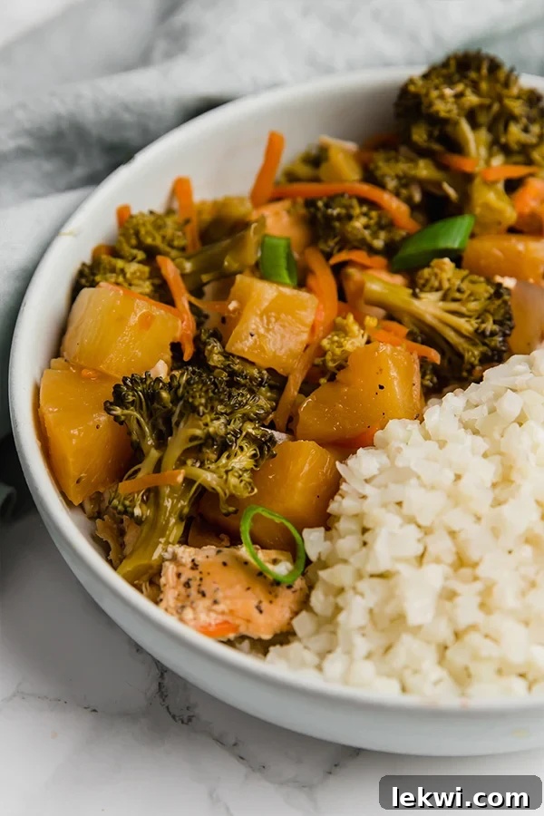 A vibrant bowl featuring tender Hawaiian chicken, juicy pineapple, and crisp vegetables served over a bed of cauliflower rice, garnished with fresh green onions.