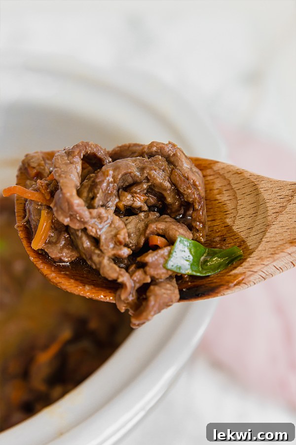 A wooden serving spoon taking a portion of cooked Mongolian beef out of the slow cooker, showing its rich sauce and tender meat.
