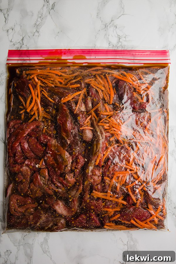 A clear plastic container filled with raw Mongolian beef ingredients, including sliced beef, carrots, and sauce, prepared for freezing.
