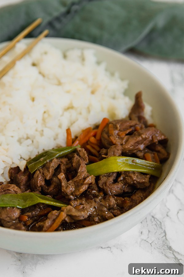 A beautifully presented bowl filled with cauliflower rice and Slow Cooker Mongolian Beef, garnished generously with fresh green onions.