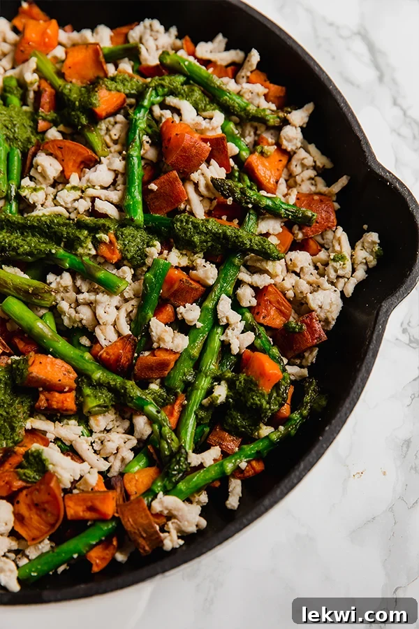 Harvest Turkey Skillet with Sweet Potatoes and Asparagus 2 A pan filled with asparagus, ground turkey, and diced sweet potatoes, garnished with fresh pesto, ready to be served.