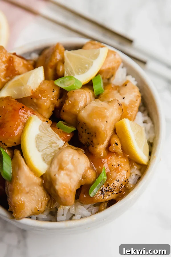 A beautifully presented bowl of healthy Chinese lemon chicken, garnished with fresh green onions, ready to be served.