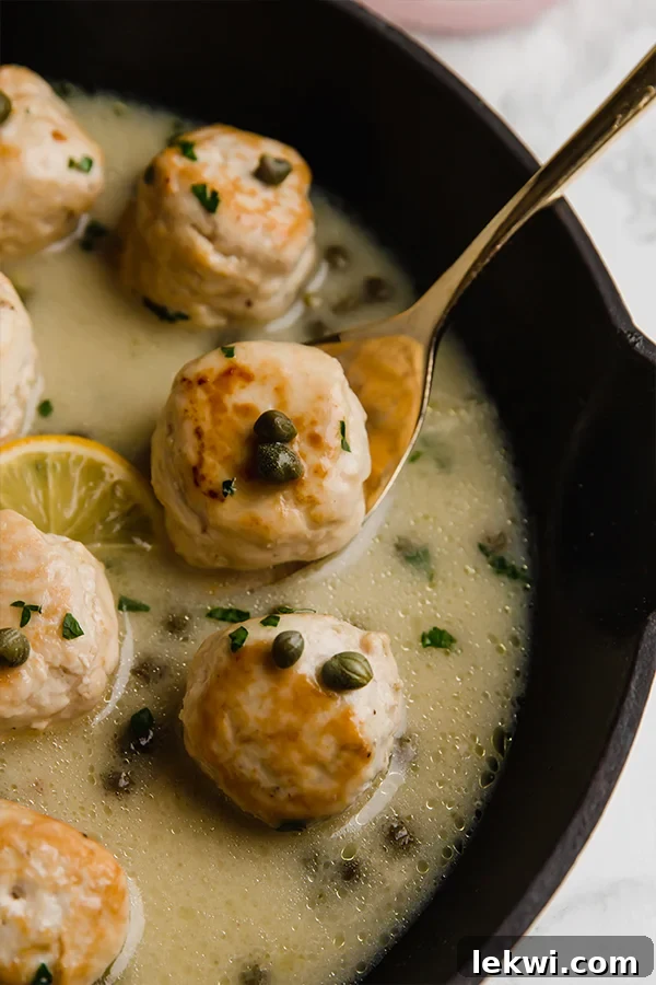 Chicken piccata meatballs in sauce in a pan with a spoon scooping out one meatball.