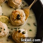 Chicken piccata meatballs in sauce in a pan with a spoon scooping out one meatball.