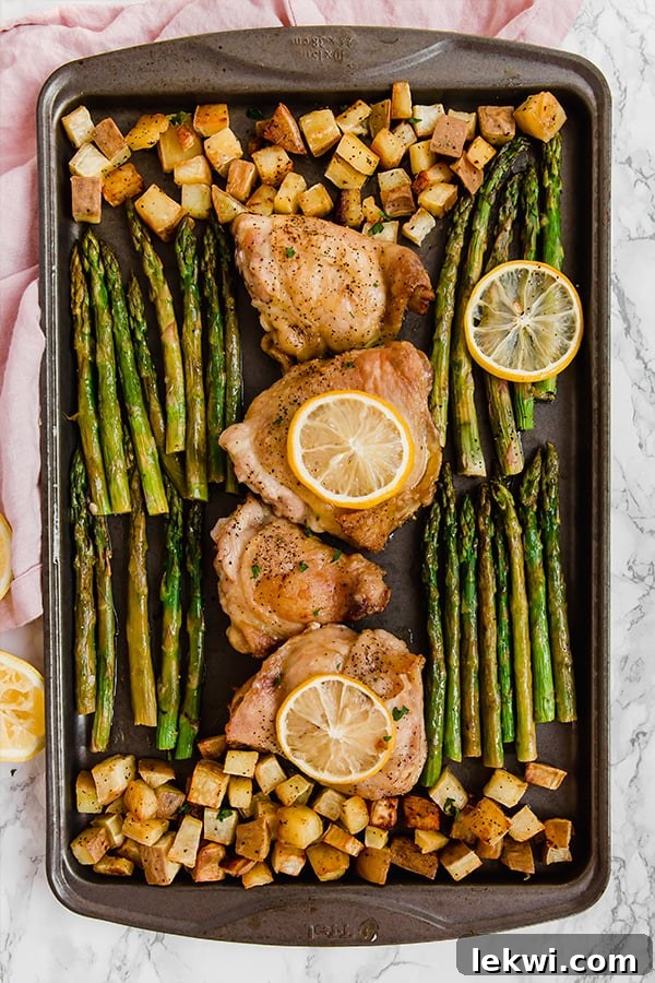 Close-up of the sheet pan with lemon chicken, sweet potatoes, and asparagus, ready for the final roast.