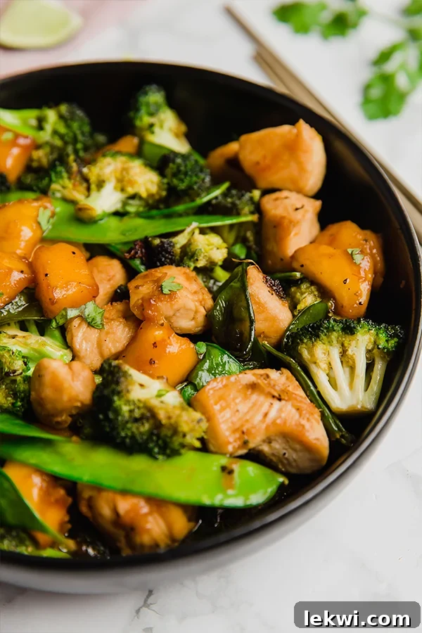 A black bowl filled with colorful mango chicken stir fry, featuring tender chicken, bright mango chunks, and crisp vegetables.