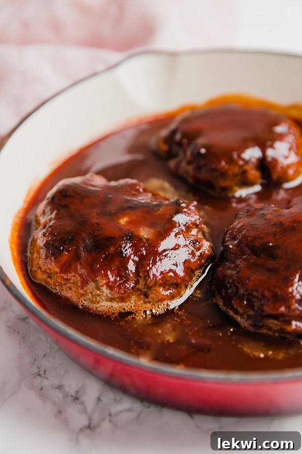 A baking dish filled with three Japanese hamburger steaks, glistening with sauce, actively cooking.