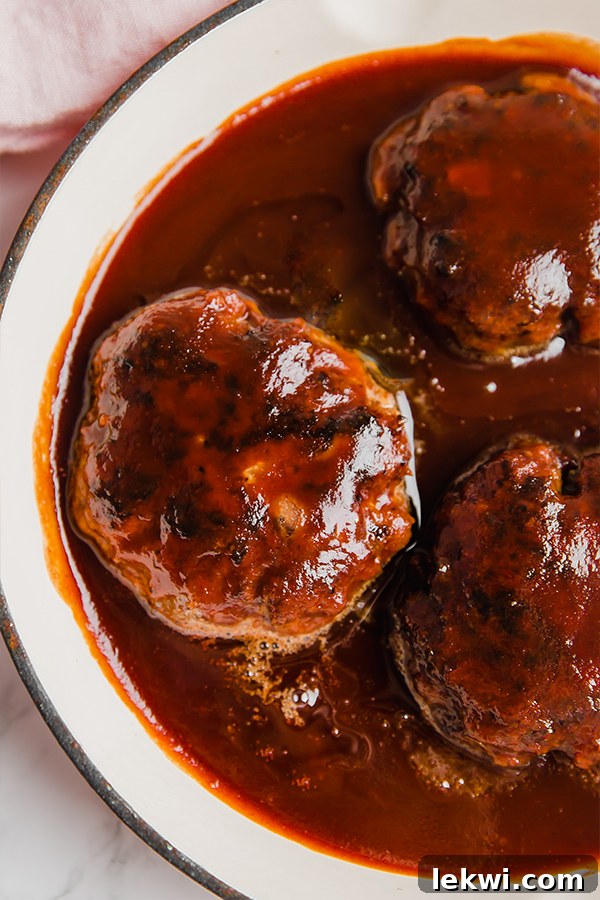 A baking dish with three Japanese hamburger steaks in it, coated in a sweet and savory sauce.