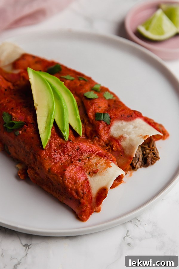 Paleo Beef Enchiladas served in a casserole dish with a single enchilada on a plate, garnished with avocado and cilantro.