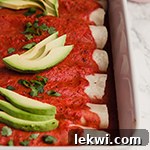 A white baking dish filled with paleo beef enchiladas topped with avocado slices.
