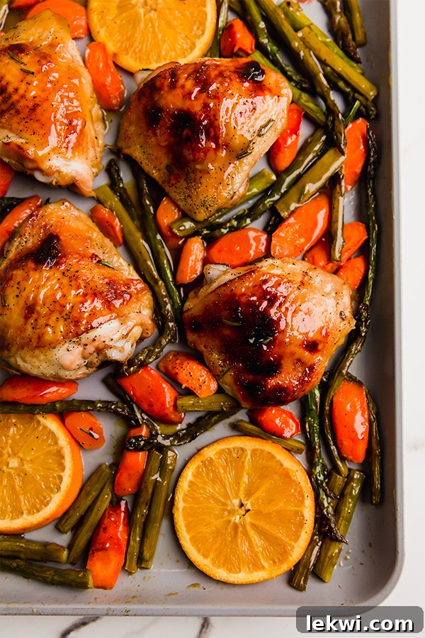 Orange glazed chicken and various vegetables beautifully arranged on a sheet pan.