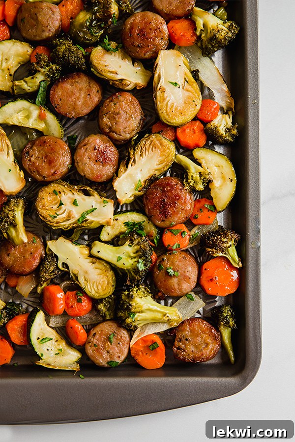 Sausage links and mixed vegetables roasting on a sheet pan.
