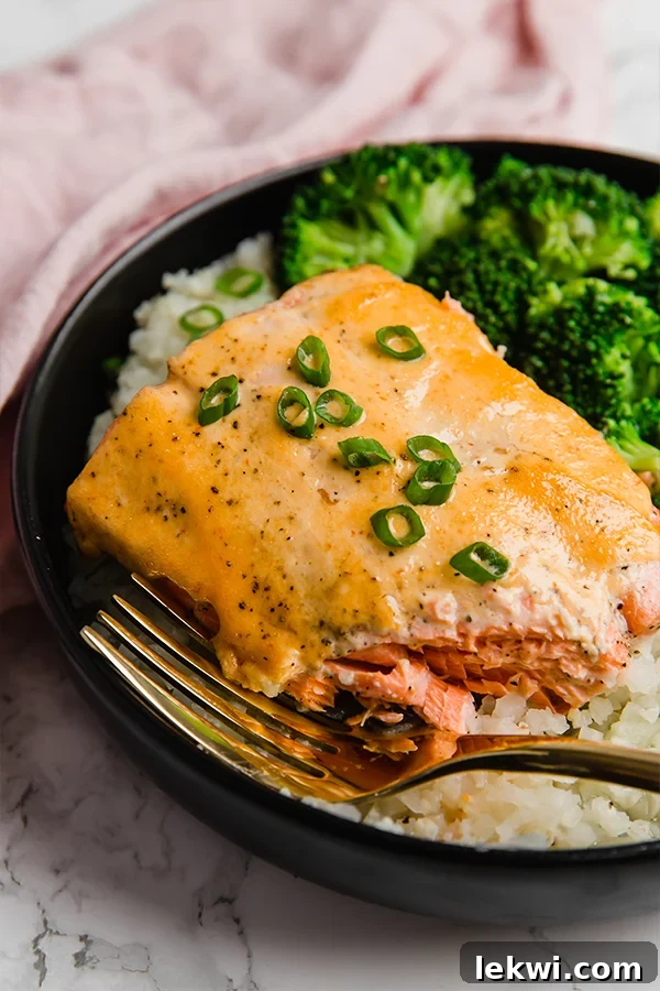 A black plate with a piece of bang bang salmon with broccoli and cauliflower rice next to it.