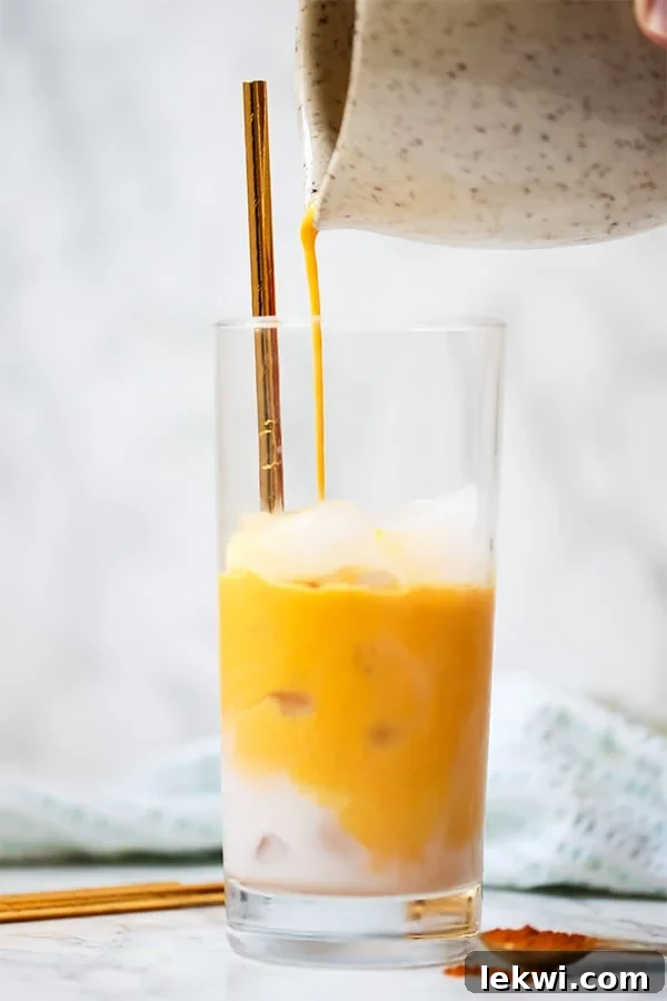 A glass of ice being filled with turmeric iced latte pouring out of a pitcher.