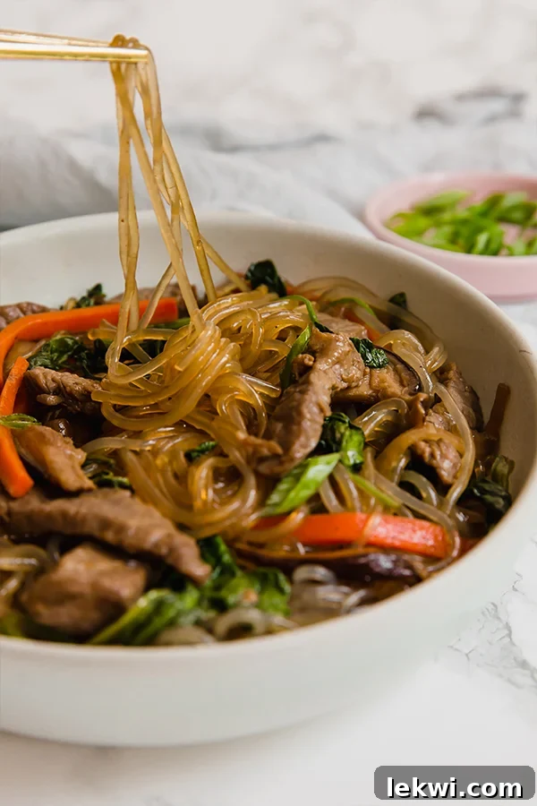 A white bowl with a serving of japchae with a few noodles being pulled out.