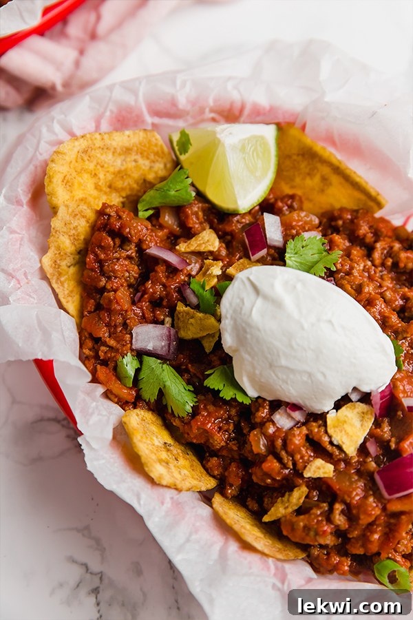 A red basket with parchment paper fille with frito pie over plantain chips with fresh lime wedges on it.
