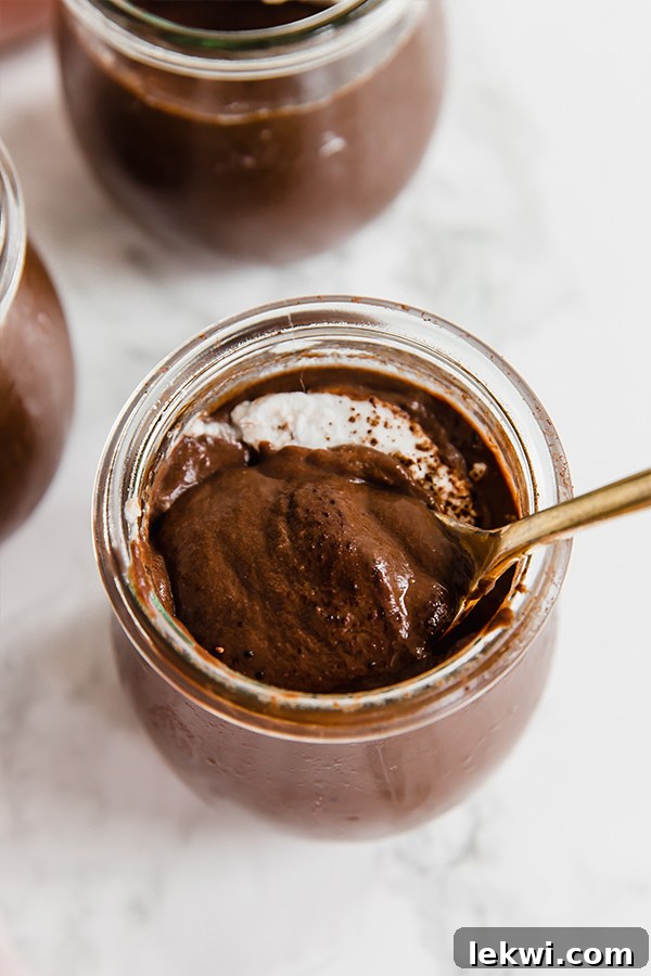 A glass jar with homemade chocolate pudding and a spoon digging into a bite.