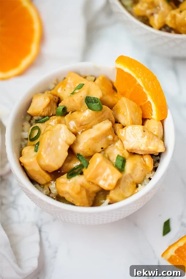A white bowl filled with slow cooker orange chicken with a wedge of fresh orange in the bowl.