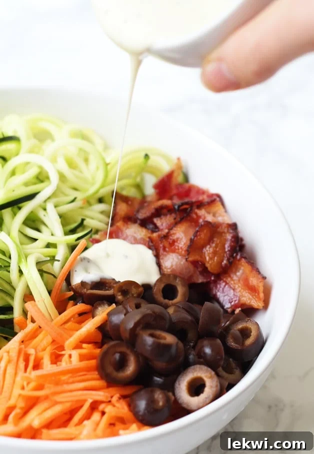 A white bowl filled with bacon ranch pasta salad with dressing being drizzled over the top.