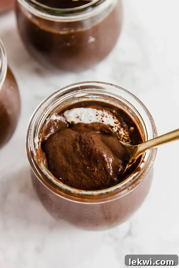 A glass jar with homemade chocolate pudding with a spoon taking a bite out.