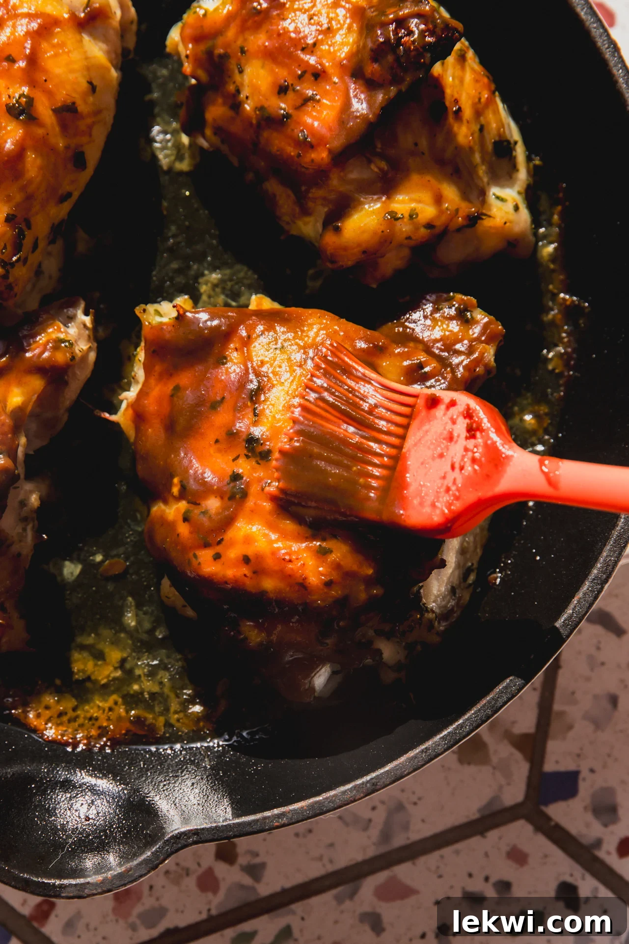 BBQ chicken in a pan with more BBQ sauce being brushed on.