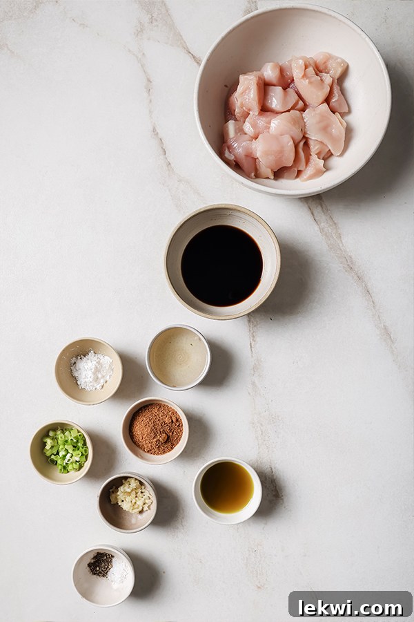 All the fresh, wholesome ingredients for crafting homemade healthy bourbon chicken bowls laid out on a rustic wooden surface before cooking, including chicken, coconut aminos, apple juice, garlic cloves, spices, and green onions.
