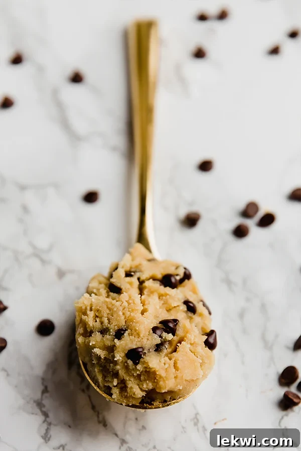A bowl of gluten-free edible cookie dough with a spoon ready to enjoy, highlighting its smooth texture and chocolate chips.