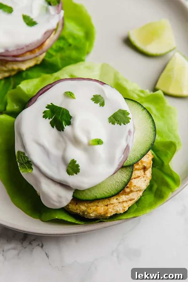 A tandoori chicken burger topped with cucumber, onions, and sauce on lettuce.