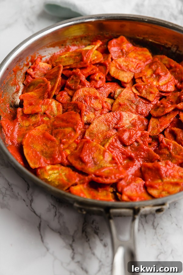A large skillet filled with plantain chilaquiles, coated in savory enchilada sauce, bubbling gently on the stovetop.