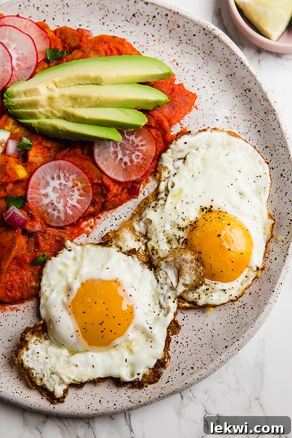 A white plate showcasing plantain chilaquiles with two perfectly fried eggs and slices of fresh avocado, creating a complete and inviting meal.