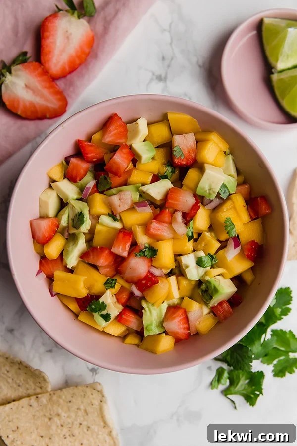 A vibrant pink bowl filled with freshly made strawberry mango salsa, featuring visible chunks of red mango, bright red strawberries, creamy green avocado, and flecks of cilantro.