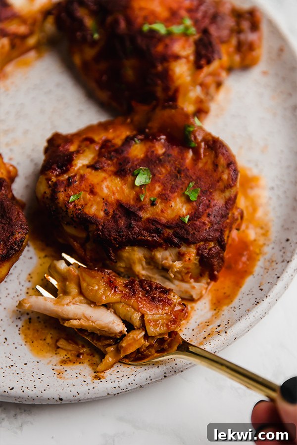 Close-up of a single BBQ chicken thigh on a rustic wooden board.
