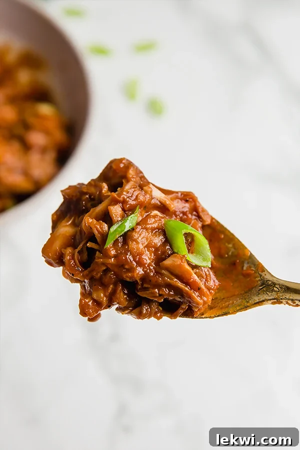 A serving spoon with a spoonful of BBQ jackfruit with green onions.