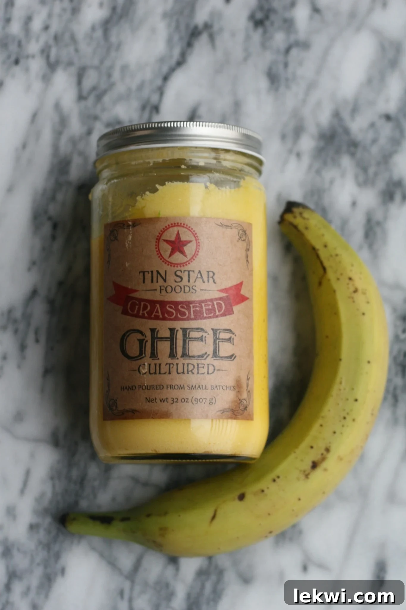 A jar of ghee and a green plantain on a kitchen counter.