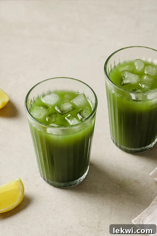 Two glasses of vibrant green matcha lemonade with lemon slices and ice.