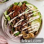 A bun less burger bowl filled with lettuce, ground beef, avocado, mushroom, and onions.