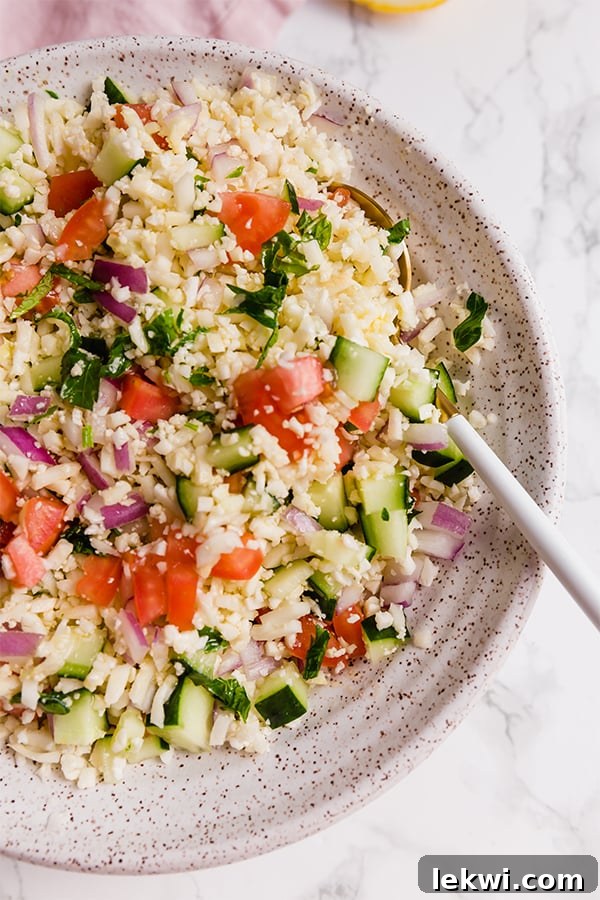 A serving bowl of grain-free cauliflower tabbouleh salad with a spoon in it, showcasing fresh ingredients.