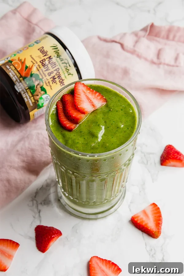 A glass with green mama smoothie in it topped with fresh strawberries.