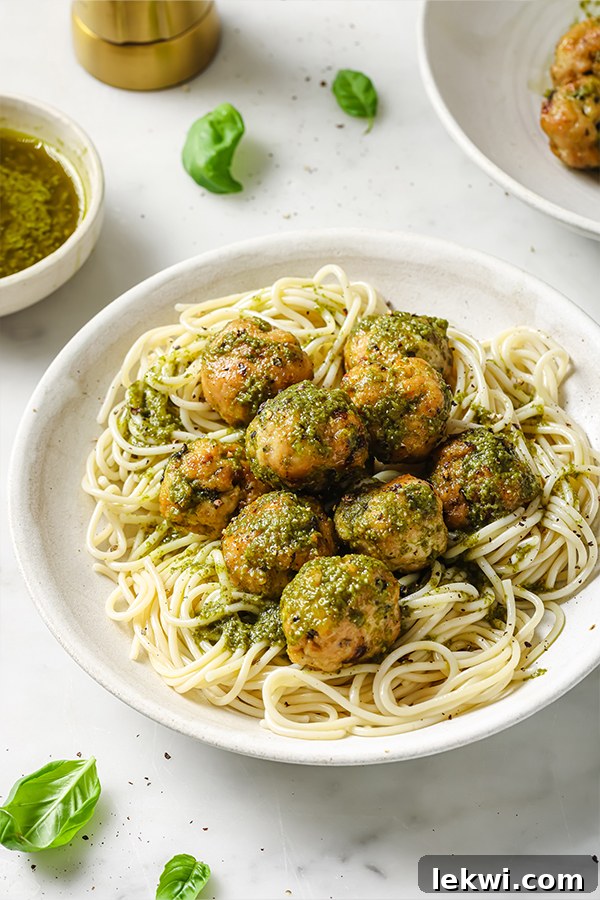 A plate of savory turkey pesto meatballs served over a bed of zucchini noodles, garnished with fresh basil and a dollop of vibrant green pesto.