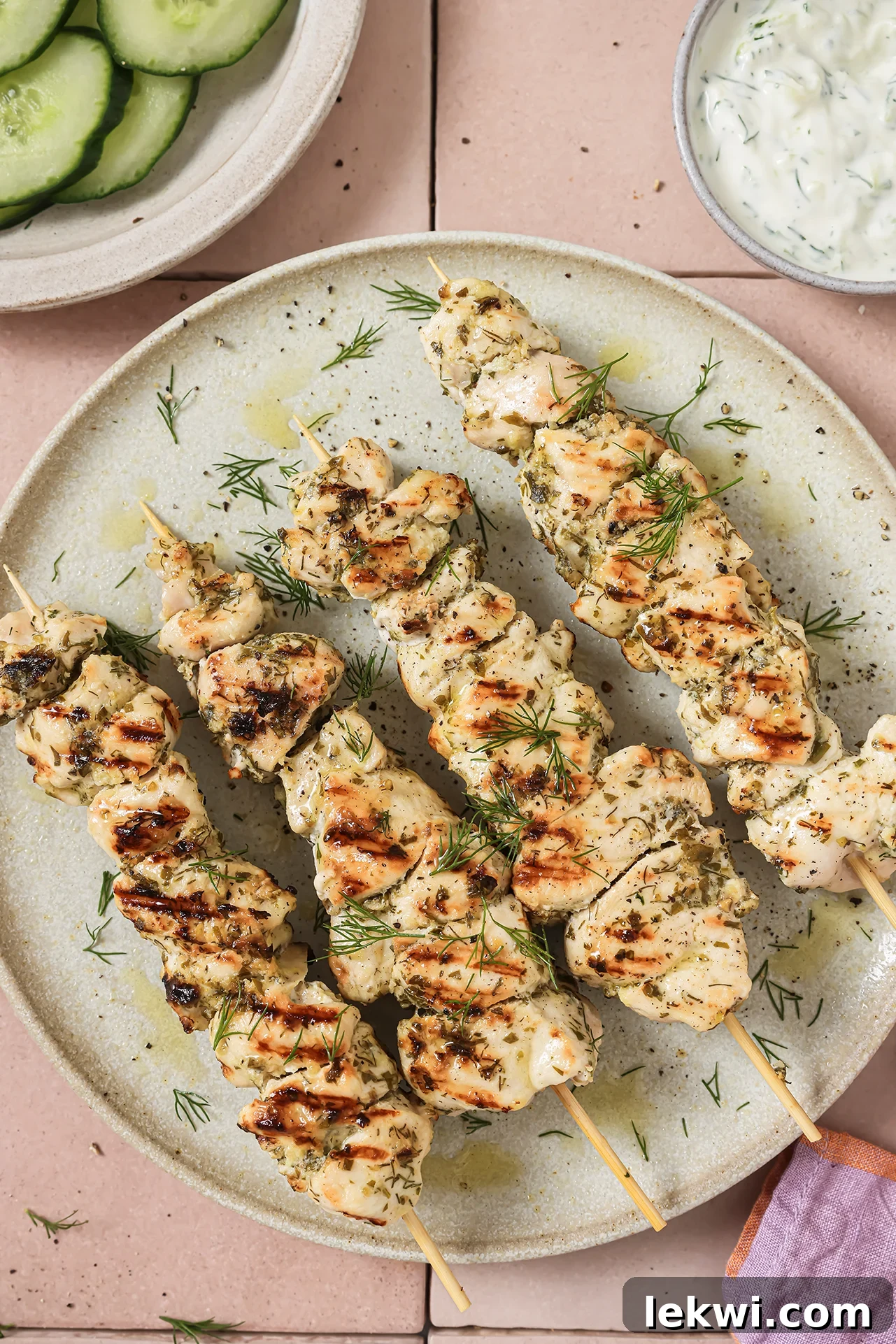 A white plate with four chicken souvlaki skewers on it, garnished with fresh herbs.