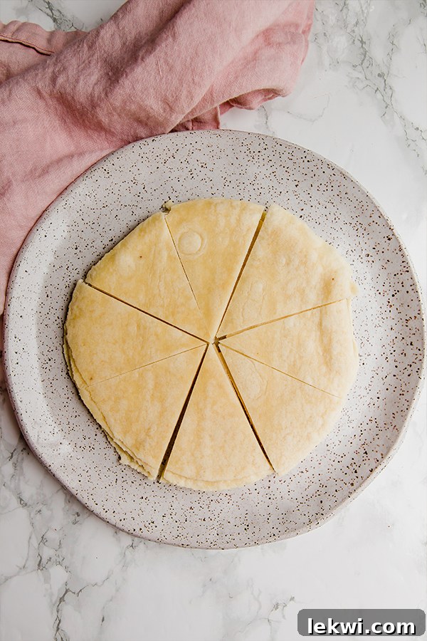 A ceramic plate holding a stack of almond flour tortillas that have been neatly cut into 8 equal wedges, ready to be prepared into cinnamon chips.