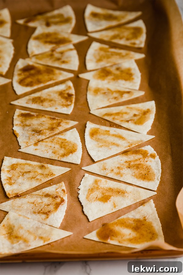 A baking sheet lined with parchment paper, showcasing raw cinnamon chips meticulously arranged in a single layer, coated with the cinnamon sugar mixture and ready for baking.