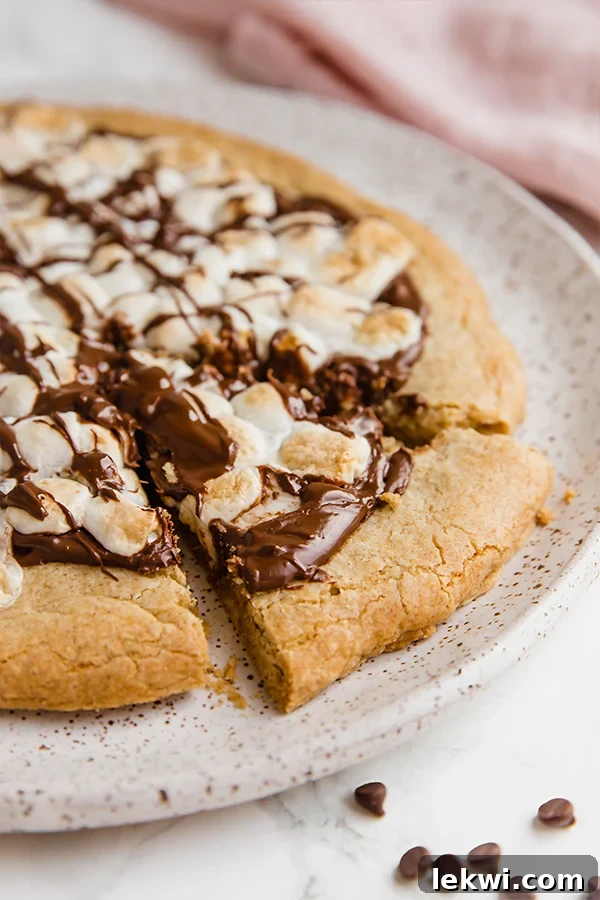 A white plate topped with s'mores pizza with one slice cut out.