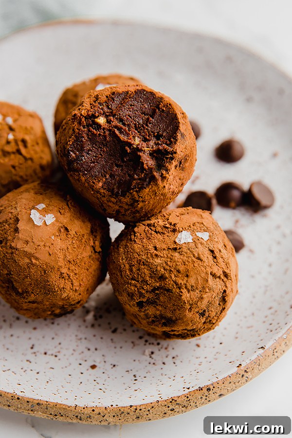 Three perfectly round chocolate avocado protein truffles dusted with cocoa powder and sea salt, artfully arranged on a ceramic dish.