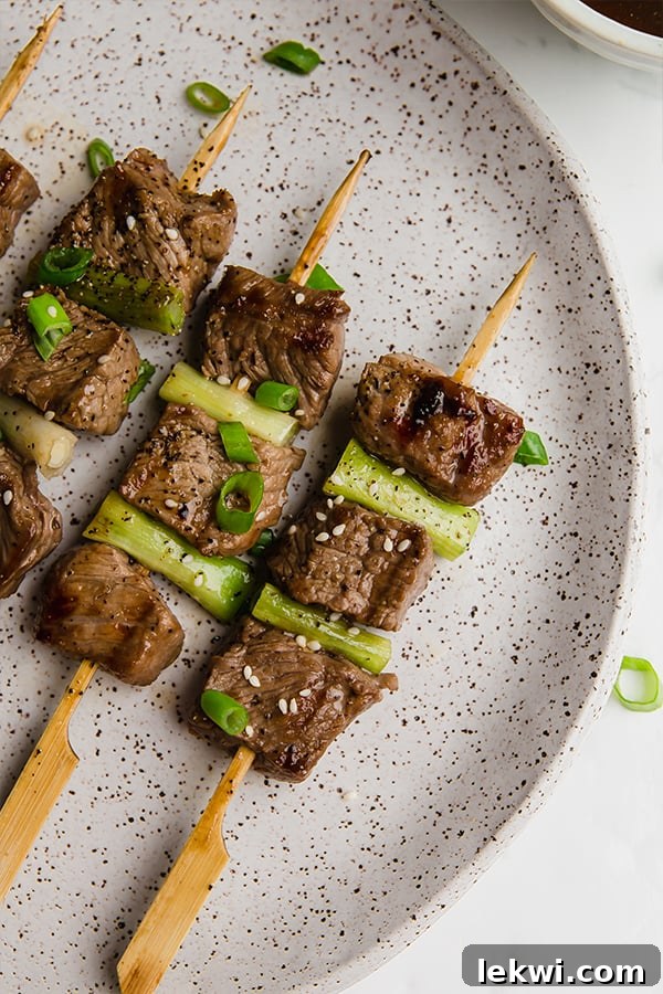 A ceramic plate with three Japanese inspired beef skewers on it.