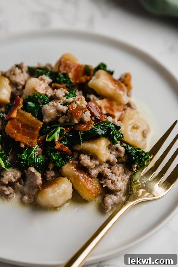 A white plate topped with gnocchi skillet and a fork nearby.